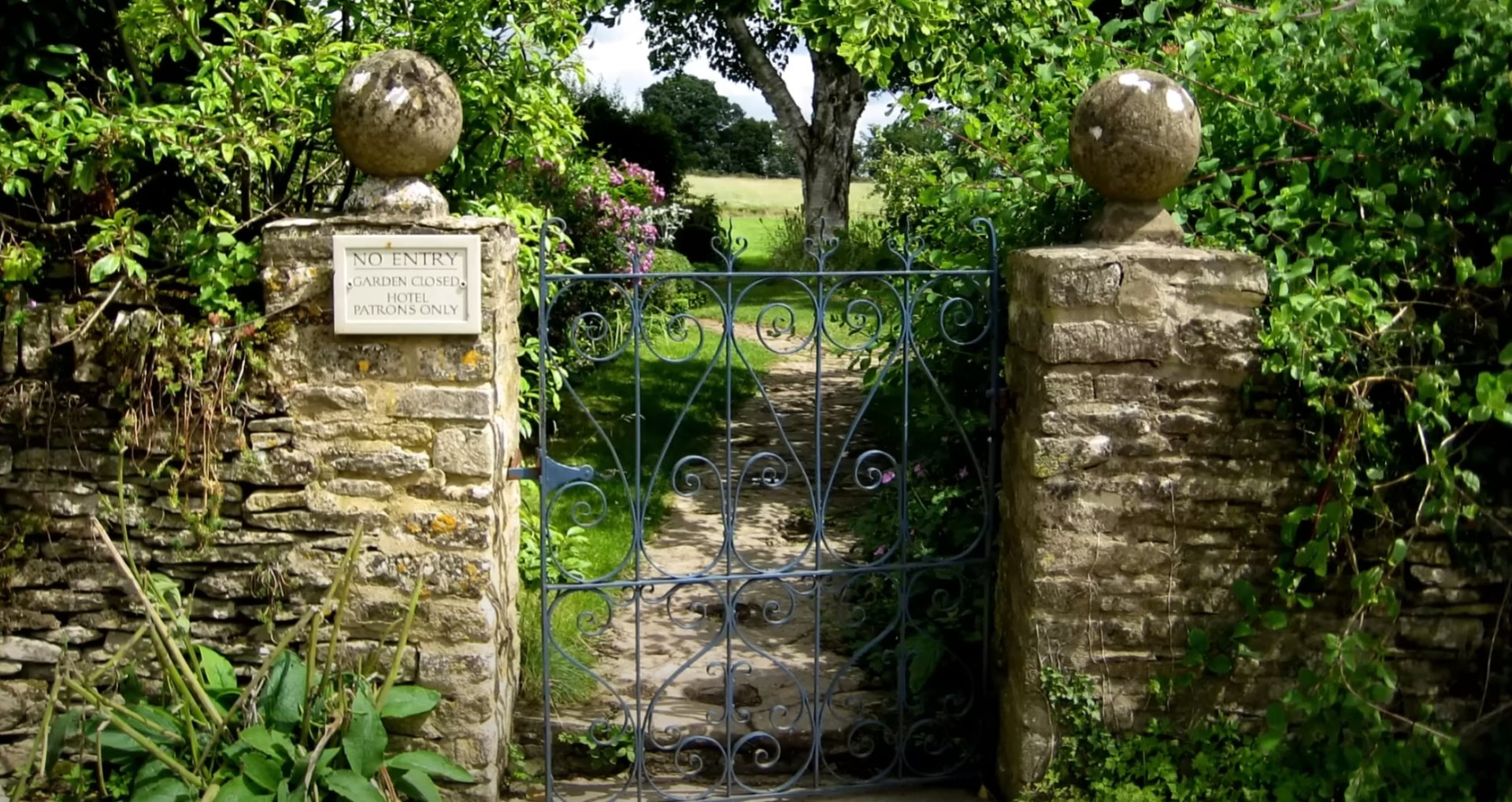 Elegant garden entrance with ornate iron gate and stone pillars surrounded by lush greenery